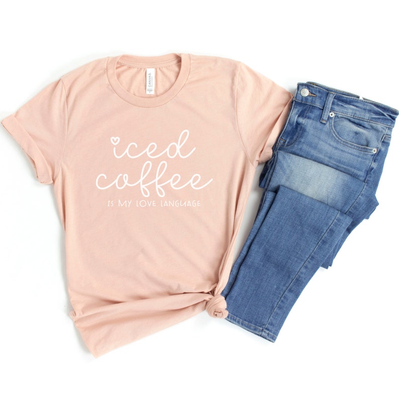 Puede incluir: Una camiseta de color melocot&oacute;n con el texto "iced coffee is my love language" en letras blancas en cursiva con un peque&ntilde;o coraz&oacute;n sobre la palabra "iced".