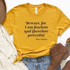 Puede incluir: Una camiseta amarilla mostaza con una cita negra que dice "Beware, for I am fearless and therefore powerful. - Mary Shelley".