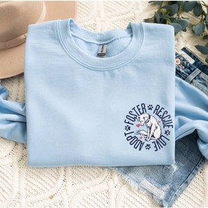 May include: Light blue sweatshirt with a graphic of a dog and the text "Foster Adopt Rescue Love" in a circle.