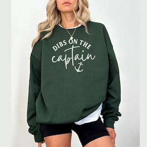 Puede incluir: Una sudadera verde oscuro con el texto "Dibs on the captain" en letras blancas y un s&iacute;mbolo de ancla.