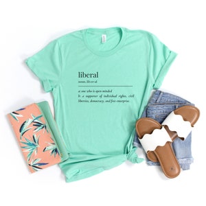 May include: A light green t-shirt with the word "liberal" defined as "one who is open-minded" and "a supporter of individual rights, civil liberties, democracy, and free enterprise."