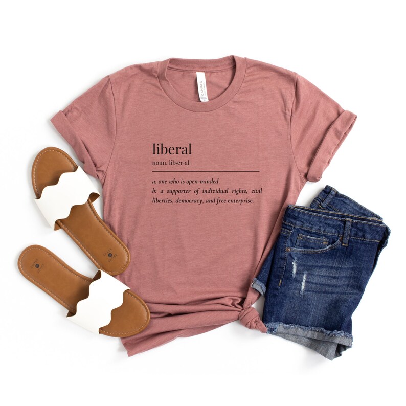 May include: A mauve t-shirt with the word "liberal" defined as "one who is open-minded" and "a supporter of individual rights, civil liberties, democracy, and free enterprise."