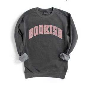 Puede incluir: Una sudadera gris oscuro con un gr&aacute;fico rosa "BOOKISH" en una fuente universitaria.