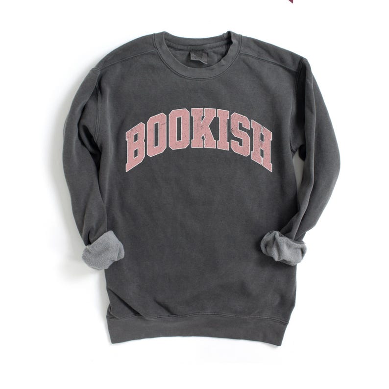 Puede incluir: Una sudadera gris oscuro con un gr&aacute;fico rosa "BOOKISH" en una fuente universitaria.
