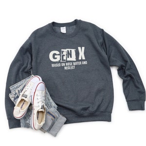 May include: A dark gray sweatshirt with the text "GEN X" in white, with the "N" in a box. The text below reads "RAISED ON HOSE WATER AND NEGLECT".