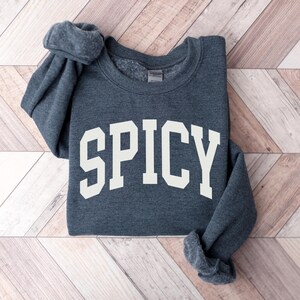 K&ouml;nnte beinhalten: Ein dunkelgrauer Pullover mit dem Wort "SPICY" in Wei&szlig; auf der Vorderseite.