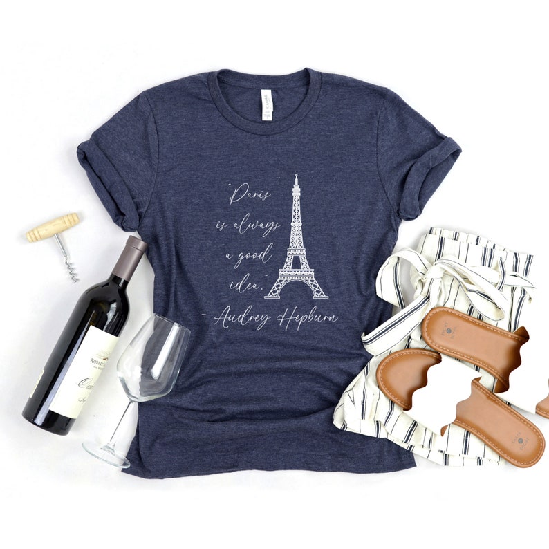 K&ouml;nnte beinhalten: Ein marineblaues T-Shirt mit einer wei&szlig;en Grafik des Eiffelturms und dem Zitat "Paris ist immer eine gute Idee. - Audrey Hepburn".