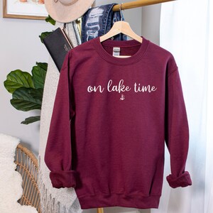 Puede incluir: Sudadera color burdeos con texto blanco que dice "on lake time" y un peque&ntilde;o s&iacute;mbolo de ancla.