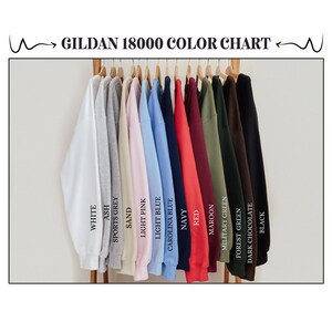 May include: Color chart for Gildan 18000 sweatshirts, showing 14 different colors: white, ash, sports grey, sand, light pink, light blue, Carolina blue, navy, red, maroon, military green, forest green, dark chocolate, and black.