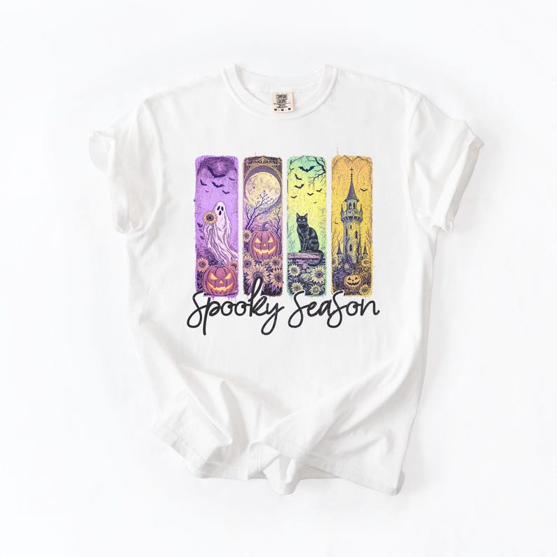 May include: White t-shirt featuring a colorful Halloween-themed design. The design includes a ghost, pumpkins, a black cat, and a spooky castle, with the words "Spooky Season" in a script font.
