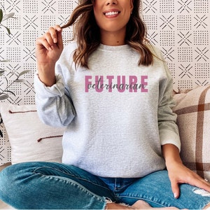 Puede incluir: Una sudadera gris con el texto "FUTURE veterinarian" impreso en rosa en la parte delantera.