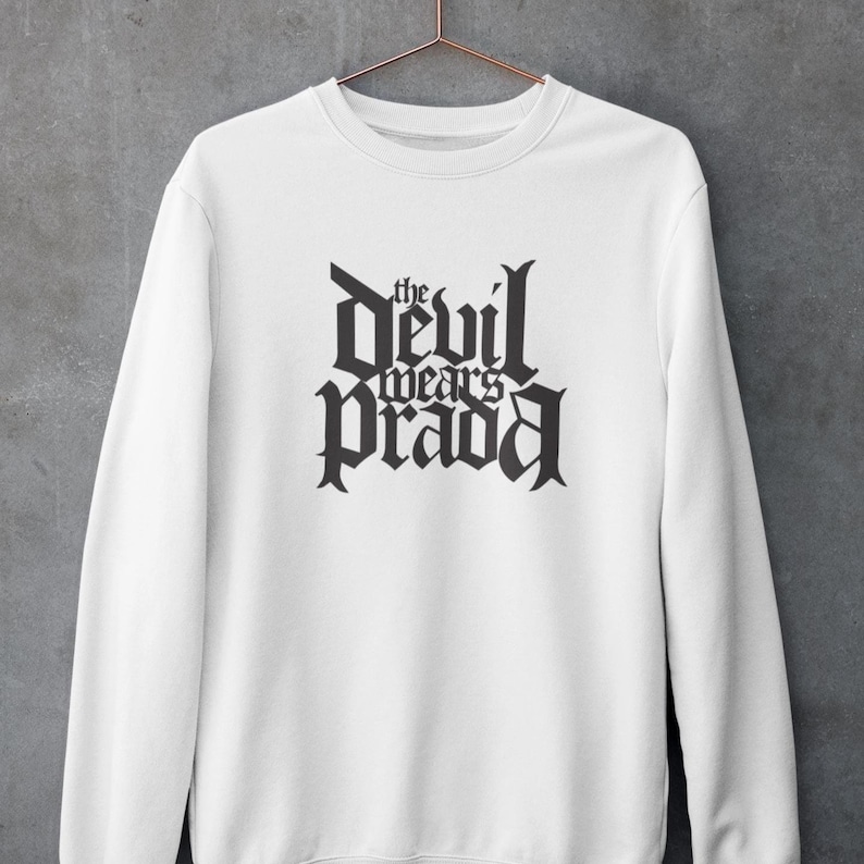 May include: White sweatshirt with black text that reads "the devil wears prada" in a gothic font.