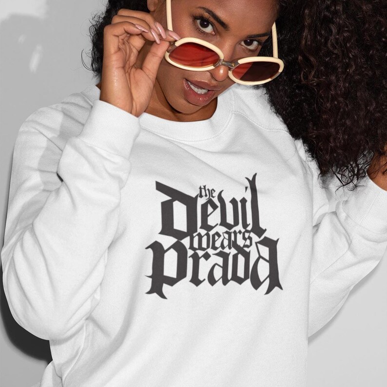 May include: White sweatshirt with a black graphic print that reads "The Devil Wears Prada" in a gothic font.