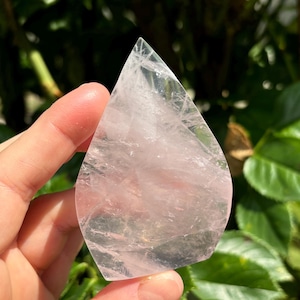 Peut inclure: Un cristal de quartz rose clair et transparent en forme de larme. Le cristal est lisse et poli, avec une légère translucidité.