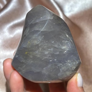 Peut inclure: Un cristal gris poli de forme lisse et arrondie. Le cristal a une qualité translucide, avec de subtiles variations de couleur et de texture. Le cristal est tenu dans une main, mettant en valeur sa taille et sa forme. Le cristal est un objet décoratif.