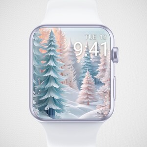 May include: A white smartwatch with a white band displays a winter forest scene with blue and peach-colored trees. The screen shows the time as 9:41 and the day as Tuesday the 12th. The watch has a silver-colored frame and a button on the side.