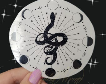 Op de afbeelding: Een witte ronde sticker met een zwart slangontwerp en een maanfasenontwerp. De slang is opgerold en heeft een sterrenpatroon. De maanfasen zijn in een cirkel rond de slang gerangschikt.