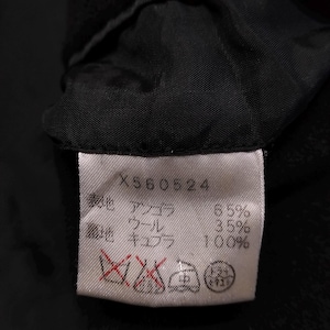 May include: A white rectangular garment care label with black text and symbols sewn into a black fabric lining. The label displays the code X560524, material composition of 65% angora and 35% wool for the outer shell, 100% cupro for the lining, and four care icons.