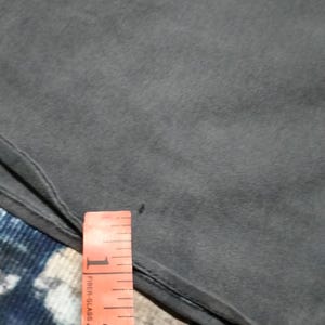 Puede incluir: Primer plano de una tela gris oscuro con una cinta m&eacute;trica naranja. La cinta tiene marcas negras y las palabras "Fiber Glass". La tela es lisa, posiblemente una prenda de vestir.
