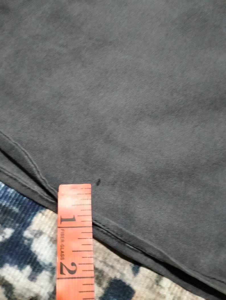 Puede incluir: Primer plano de una tela gris oscuro con una cinta m&eacute;trica naranja. La cinta tiene marcas negras y las palabras "Fiber Glass". La tela es lisa, posiblemente una prenda de vestir.