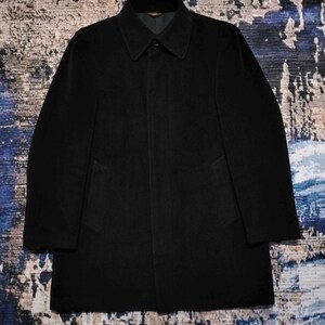 May include: A solid black coat featuring a structured collar, long sleeves, and a concealed button placket. The garment has a clean, minimalist silhouette with two side pockets and a smooth, dark fabric finish, presenting a classic design.