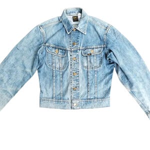 May include: Light blue denim jacket with a button-down front, two chest pockets, and gold-colored buttons. The jacket has a classic collar and long sleeves. The Lee logo is visible on the chest pocket.
