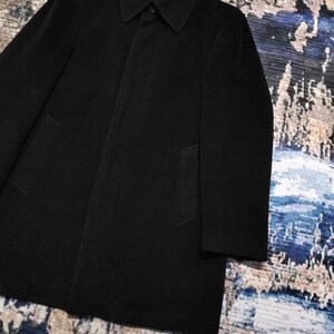 May include: A solid black overcoat featuring a structured collar, long sleeves, and a concealed button placket. The coat has a smooth, matte finish and a clean, straight silhouette that extends to the mid-thigh, providing a classic and simple look.