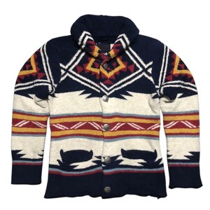 May include: A button-up cardigan sweater with a shawl collar. The sweater features a geometric pattern in navy blue, cream, red, and yellow. It has two front pockets and silver-colored buttons.