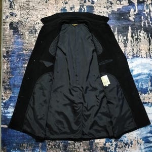 May include: A black coat with a wide collar and long sleeves, shown open to reveal a dark interior lining. The garment features quilted shoulder panels and a small white rectangular tag on the inside right panel with the text AAR printed on it.