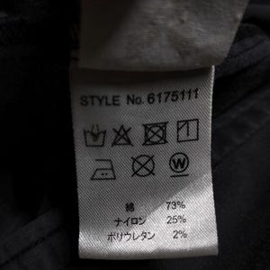 Puede incluir: Primer plano de una etiqueta de ropa con el texto "STYLE No. 6175111". La etiqueta muestra s&iacute;mbolos de cuidado y la composici&oacute;n de la tela: 73% algod&oacute;n, 25% nailon y 2% poliuretano.