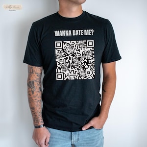 Op de afbeelding: Een zwart T-shirt met de tekst "Wanna Date Me?" en een zwart-witte QR-code gedrukt op de voorkant.