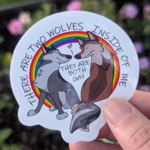 May include: A circular sticker featuring two cartoon wolves, one grey and one brown, standing before a rainbow. The text reads: THERE ARE TWO WOLVES INSIDE OF ME THEY ARE BOTH GAY. A small pink heart is positioned between the wolves' noses.