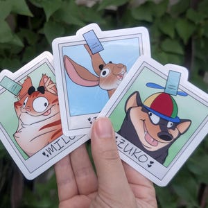 May include: Three square stickers designed like polaroid photos. One features an orange tabby cat labeled MILO, one shows a brown rabbit, and one depicts a black and tan dog wearing a propeller hat labeled ZUKO. Each has a small blue tab at the top.