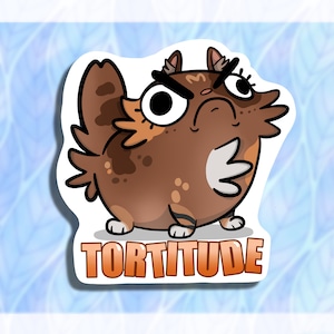 May include: A cartoon illustration of a brown, orange, and white cat with a grumpy expression. The cat is looking to the right and has its right paw raised. The text "TORTITUDE" is written in orange letters below the cat.