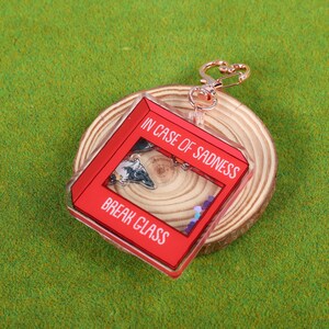 May include: Red acrylic keychain with a clear window that says "In case of sadness, break glass". The keychain is attached to a gold-colored metal ring.