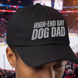 May include: Black baseball cap with the text "HIGH-END GAY DOG DAD" embroidered in white. The cap has a curved brim and a fabric strap closure. The hat is a classic six-panel design.