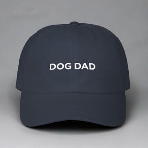 May include: Navy blue baseball cap with the white text "DOG DAD" embroidered on the front. The cap has a curved brim and an adjustable strap at the back. A casual accessory for dog lovers.