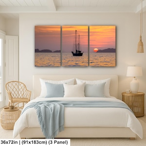 Op de afbeelding: Een drieluik canvas print met een zonsondergang boven de oceaan. Het kunstwerk toont een silhouet van een zeilboot op het water, met een oranje en gele lucht. Afmetingen: 91x183cm.