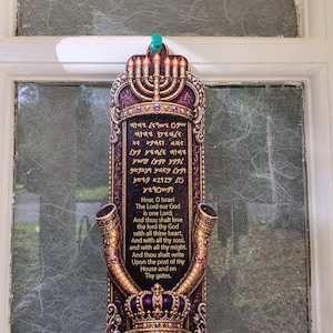 May include: A vertical rectangular wall plaque in deep purple and gold featuring a menorah at the top and a crown at the bottom. The center displays the Shema Yisrael prayer in Hebrew and English text, flanked by two shofar horns on the sides.