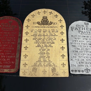 May include: Three decorative wooden plaques with religious inscriptions. The plaques are in red, gold, and gray. The red plaque reads "Our Father's Prayer" and the gray plaque reads "Pray Without Ceasing". The gold plaque reads "10 Commandments".