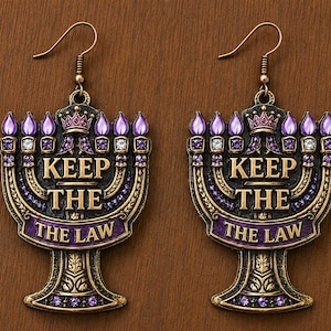 May include: A pair of bronze-toned metal earrings shaped like a menorah, featuring purple enamel accents, small clear and purple crystals, and a crown detail. The text KEEP THE THE LAW is embossed in the center of each earring with hook backings.