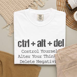Könnte beinhalten: Ein weißes kurzärmeliges T-Shirt mit dem schwarzen Text ctrl + alt + del, gefolgt von den Worten Control Yourself, Alter Your Thinking, Delete Negativity. Das T-Shirt hat einen Rundhalsausschnitt und ein Comfort Colors Markenetikett am Kragen.