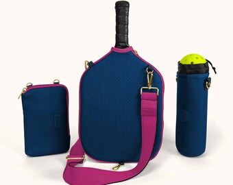 May include: A blue and pink pickleball paddle bag with a matching phone case and ball holder. The bag has a shoulder strap and a zipper closure.