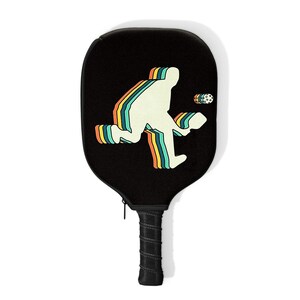 May include: A black pickleball paddle with a retro-style silhouette of a player in a rainbow design. The paddle has a black handle with a zipper.