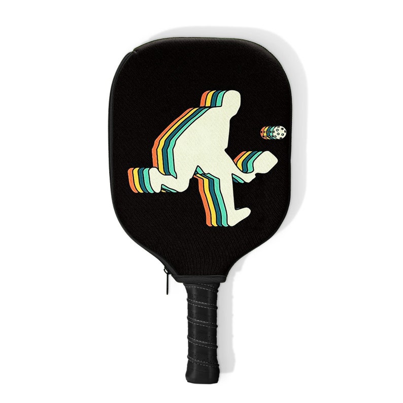 May include: A black pickleball paddle with a retro-style silhouette of a player in a rainbow design. The paddle has a black handle with a zipper.