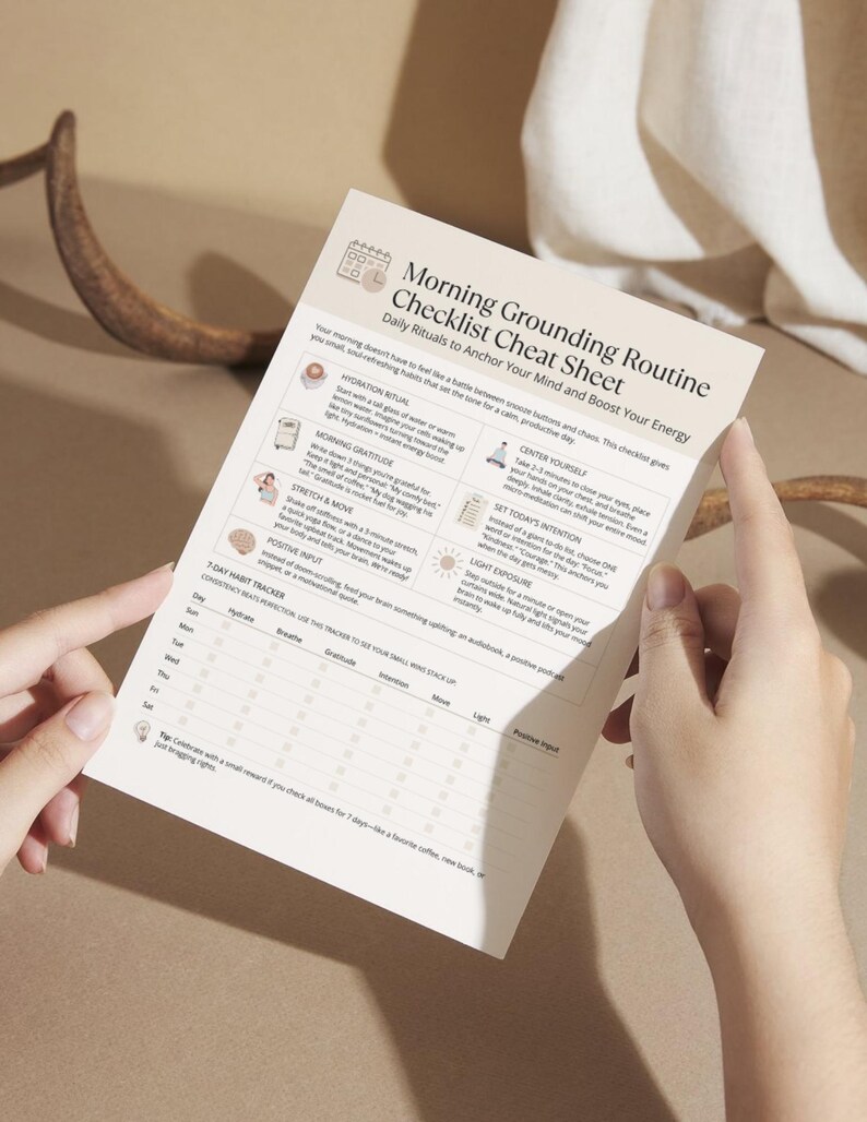 Hands holding a printed copy of the Morning Grounding Routine Checklist cheat sheet with clear sections for rituals and a weekly tracker.