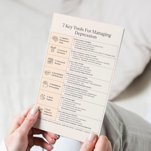 Mood support depression worksheet held in hands over white bedding, printable mental health resource for self-care and healing.