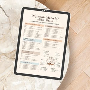 May include: A digital tablet displays a "Dopamine Menu for ADHD Brain" guide. The white screen features text and diagrams outlining strategies for energy and motivation, including quick boosts and reward tasks. The tablet rests on a light-colored, textured surface.