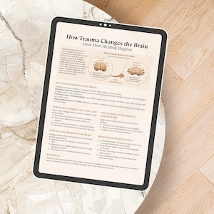 May include: A digital tablet displays a detailed infographic titled "How Trauma Changes the Brain." The text and diagrams explain the impact of trauma on the brain and the healing process. The tablet rests on a light-colored, patterned surface.
