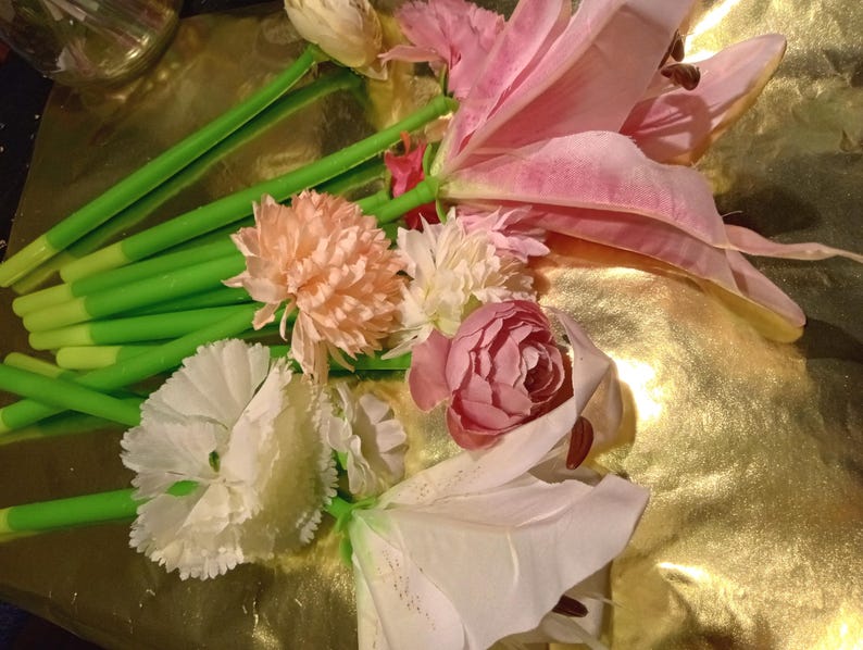 May include: A collection of pens topped with artificial flowers in various shades of pink, white, and peach. Each pen features a bright green stem-like barrel and a realistic fabric floral bloom attached to the top, creating a bouquet-like appearance.